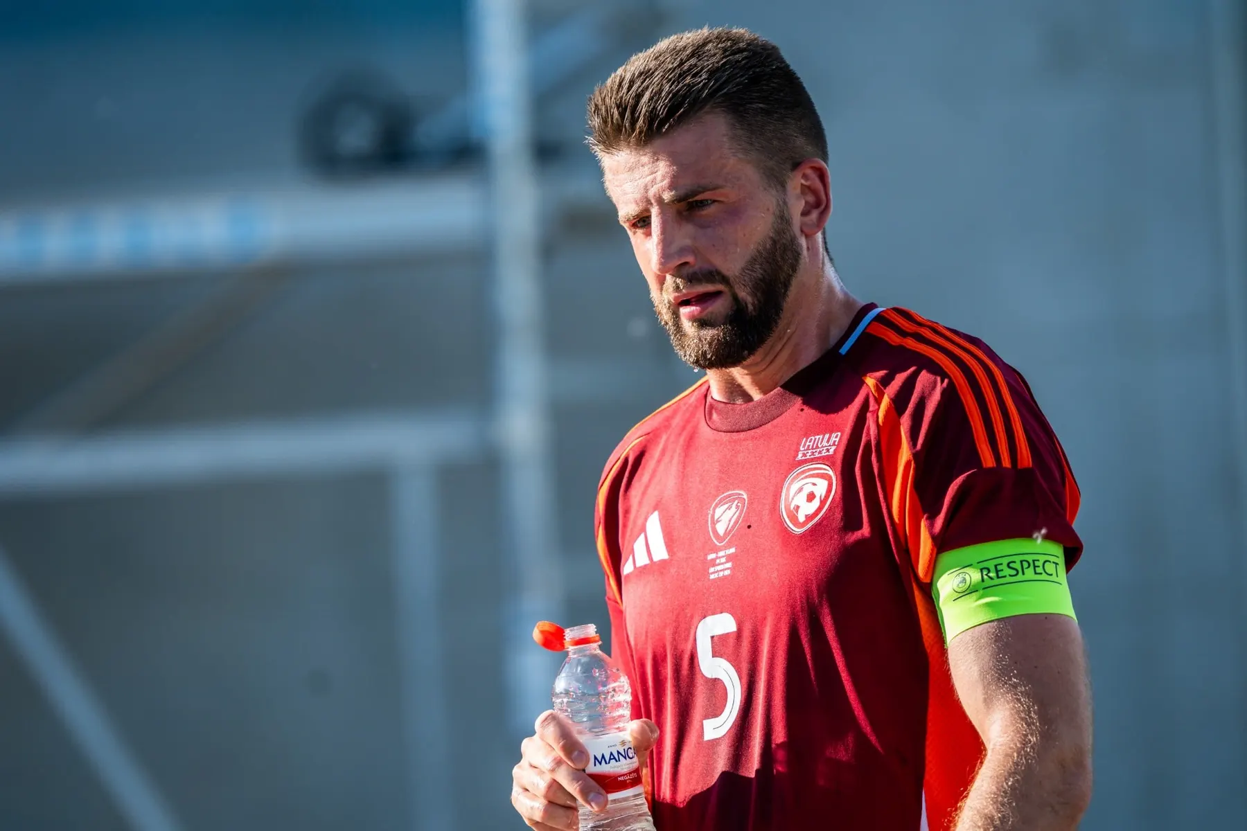 A Latvian national team player wearing the captain's armband on a sunny day