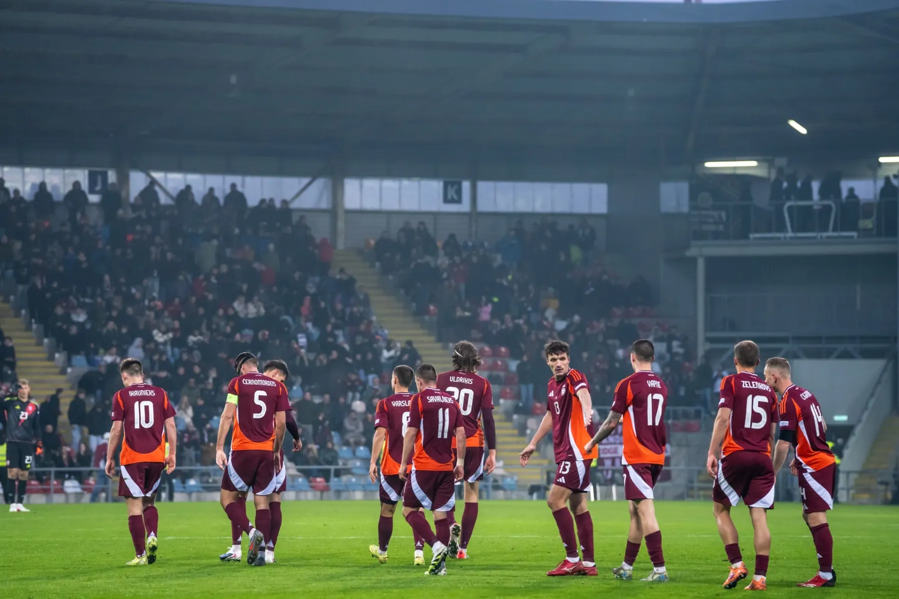Latvian national team players in burgundy kits walking across the pitch in front of full stands